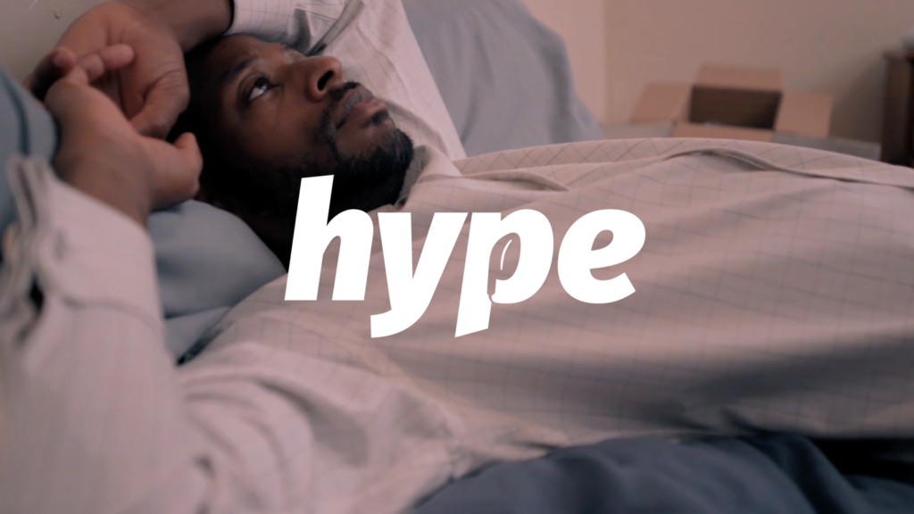 Main Character of hype in a white shirt, laying n blue sheets. The word "Hype" is written is white lettering